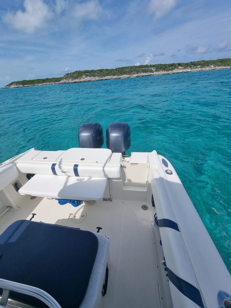 Staniel Cay, Exuma Bahamas Boat with dual engines on clear turquoise water, approaching a lush green island under a partly cloudy sky.