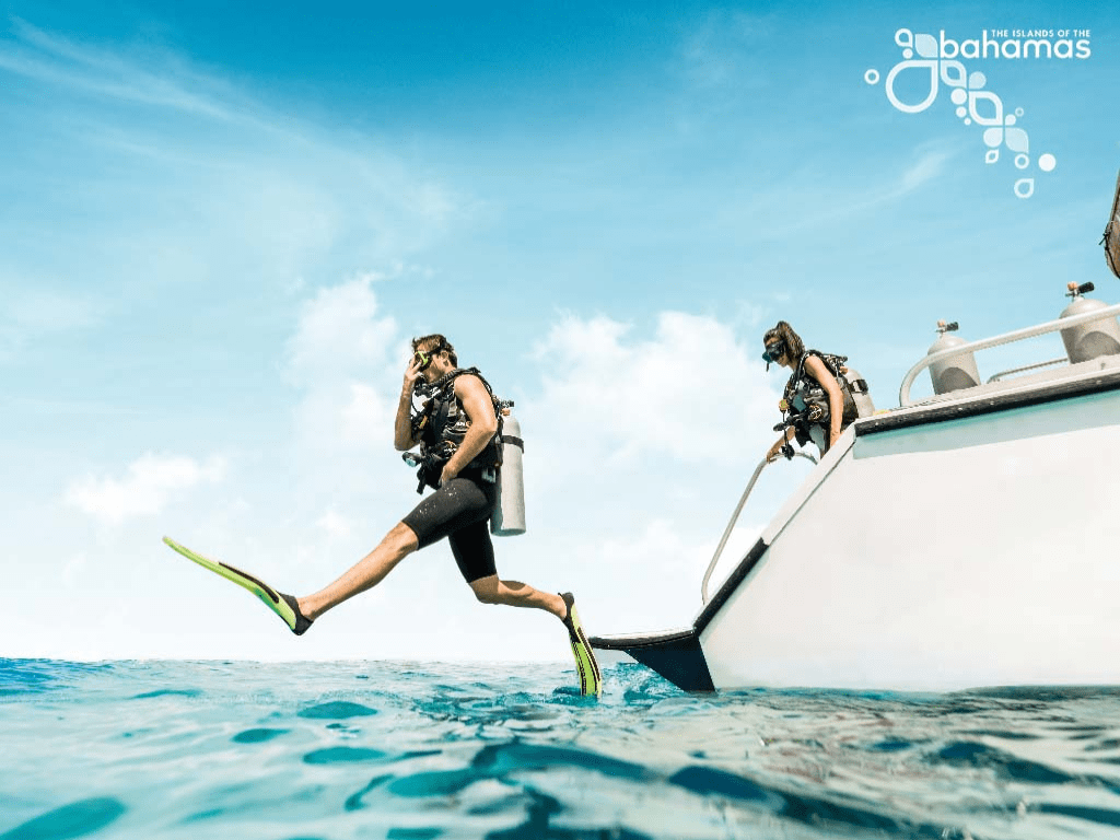 Two people from Staniel Cay Adventures scuba diving off a boat in the ocean.