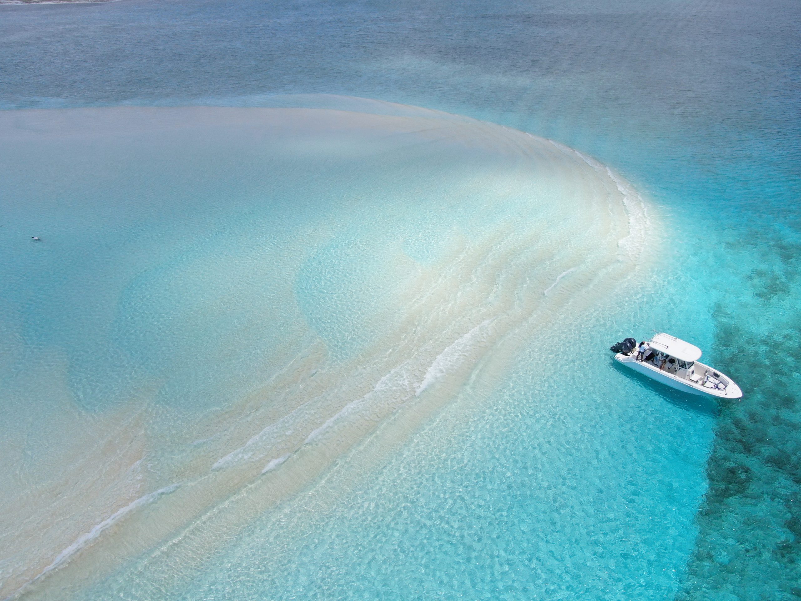 An aerial view of a boat in the water near a white sand beach during the Fishing Staniel Cay adventure.