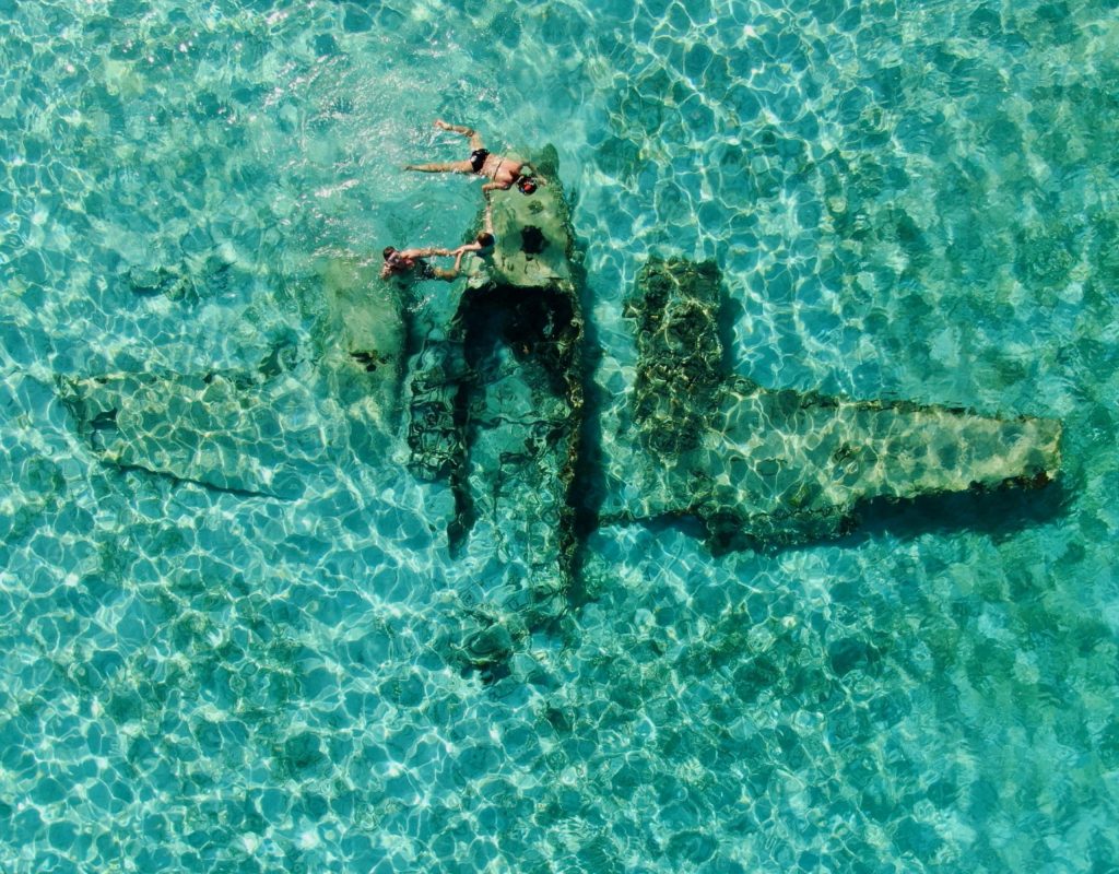 Staniel Cay, Exuma Bahamas Aerial view of a submerged airplane wreck in clear turquoise water, with a person snorkeling above it.