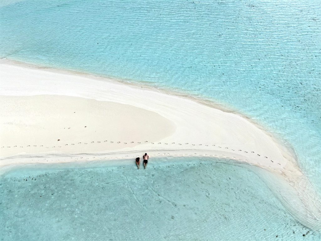 Two people walking on a white sand island in the Maldives, enjoying the beauty of Staniel Cay Adventures.