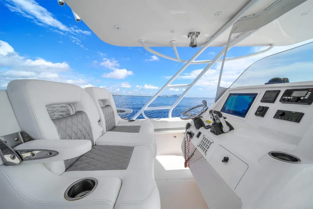 Staniel Cay, Exuma Bahamas Cockpit of a modern boat featuring two white cushioned seats, a control panel with electronic displays, and ocean visible under a partly cloudy sky. Swimming Pigs Tours, Fishing and more!