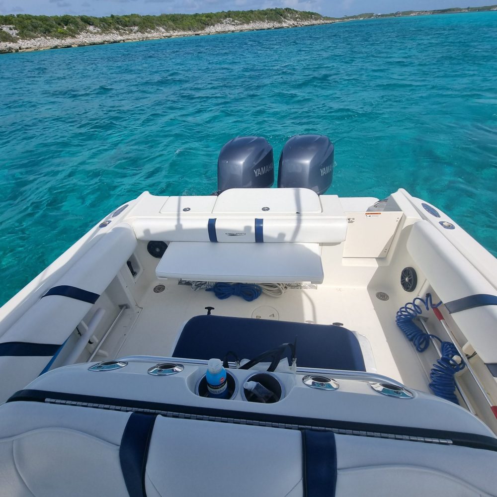 Staniel Cay, Exuma Bahamas A boat with two motors and a seating area is on clear turquoise water. The shoreline and a cloudy sky are visible in the background.