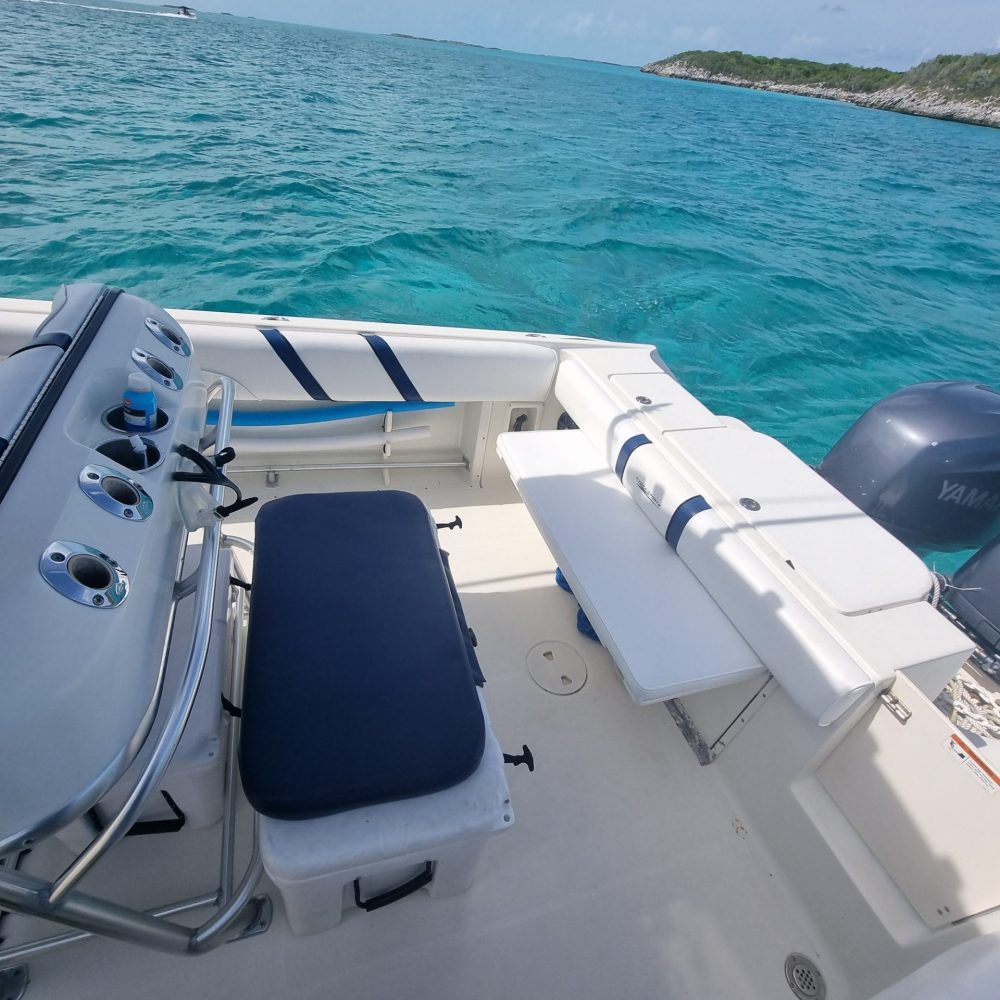 Staniel Cay, Exuma Bahamas Boat interior with seating and controls, floating on clear blue water near a distant green shoreline under a cloudy sky.