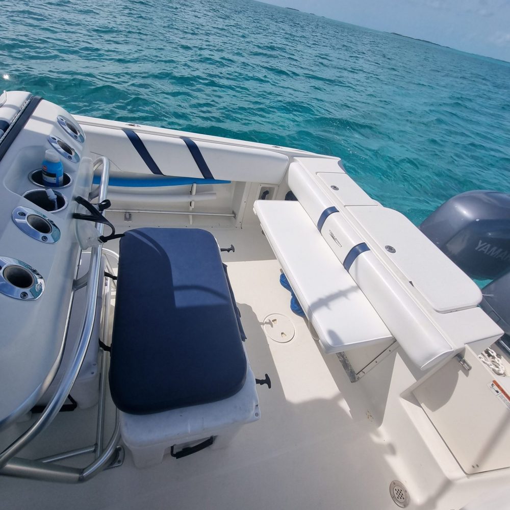 Staniel Cay, Exuma Bahamas View of a boat's deck with a seating area and fishing rod holders, surrounded by calm blue ocean under a partly cloudy sky.