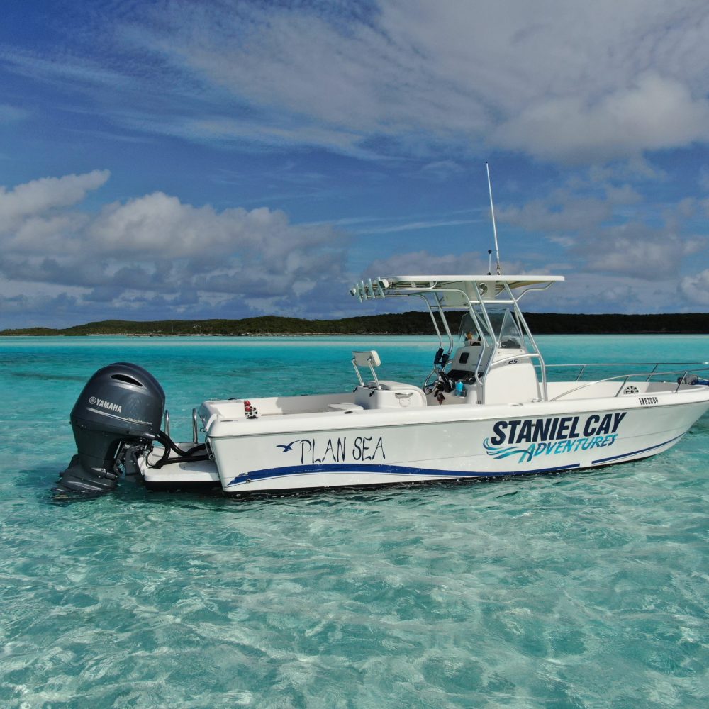 Staniel Cay, Exuma Bahamas A white boat labeled "Staniel Cay Adventures" floats on clear turquoise water under a blue sky with clouds.