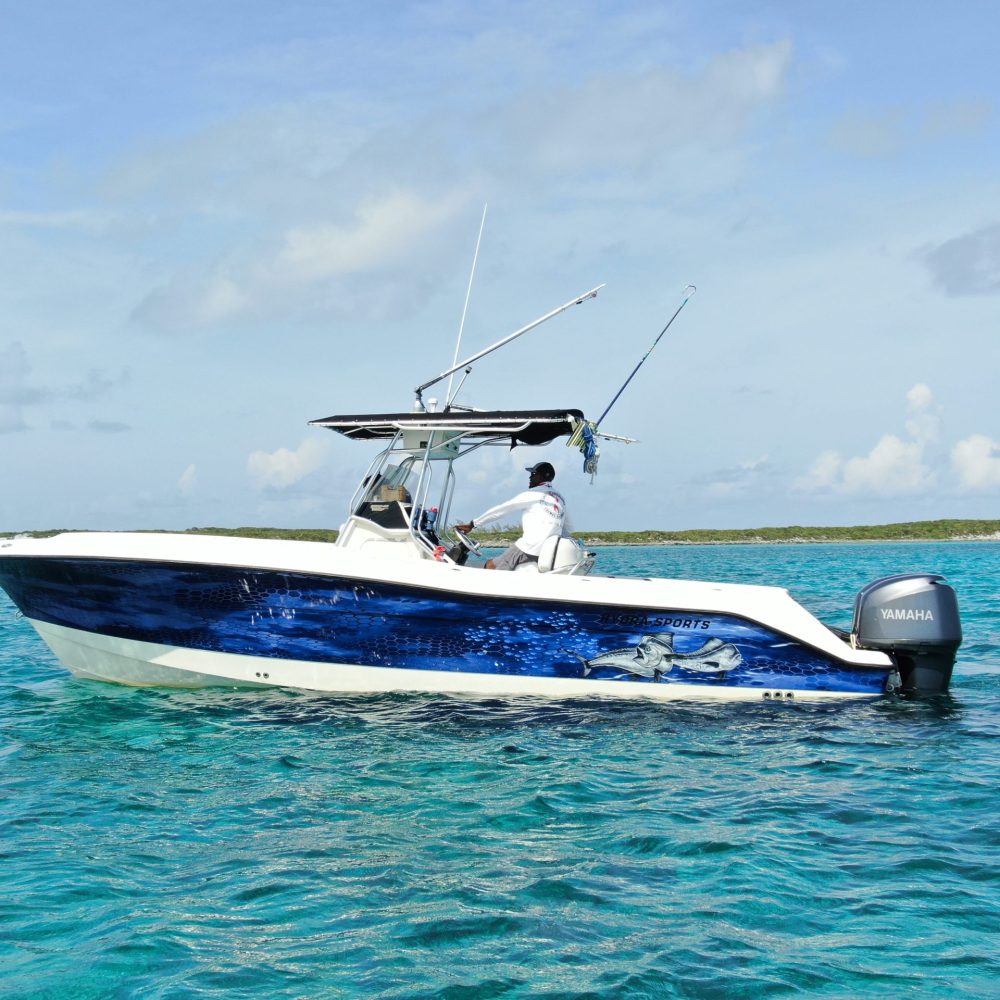 Staniel Cay, Exuma Bahamas A person steering a white and blue speedboat with fishing rods on a calm, turquoise sea under a clear sky.