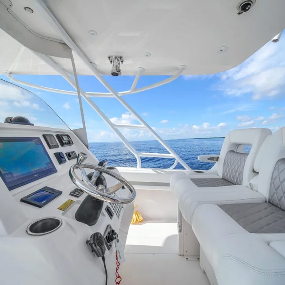 Staniel Cay, Exuma Bahamas View of a boat's helm with steering wheel, navigation screens, and white cushioned seats, set against a backdrop of blue ocean and sky. Swimming Pigs Tours, Fishing and more!