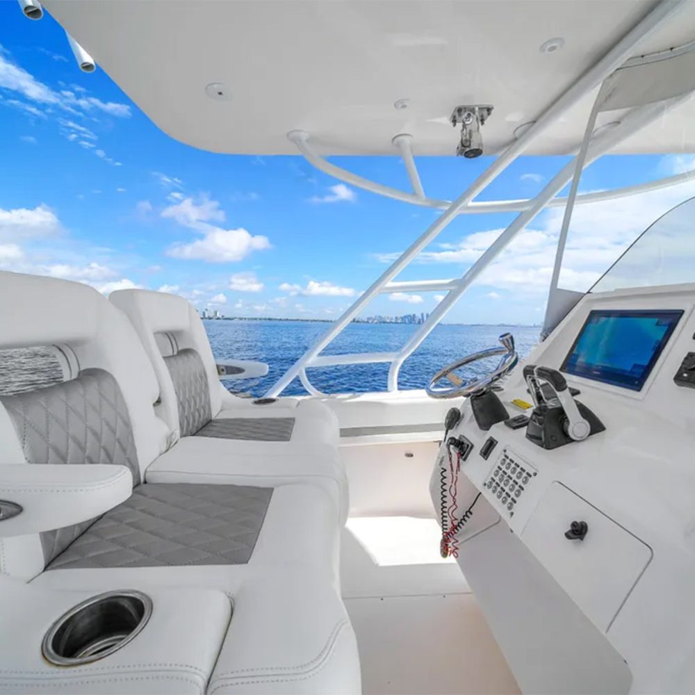 Staniel Cay, Exuma Bahamas Cockpit of a modern boat featuring two white cushioned seats, a control panel with electronic displays, and ocean visible under a partly cloudy sky. Swimming Pigs Tours, Fishing and more!