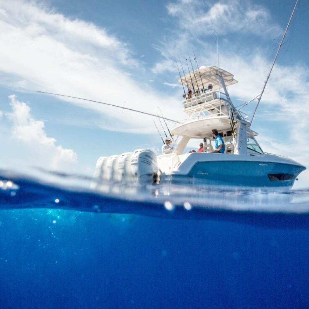 Staniel Cay, Exuma Bahamas A white boat floats on clear blue water under a partly cloudy sky, with an underwater view of the ocean's surface.