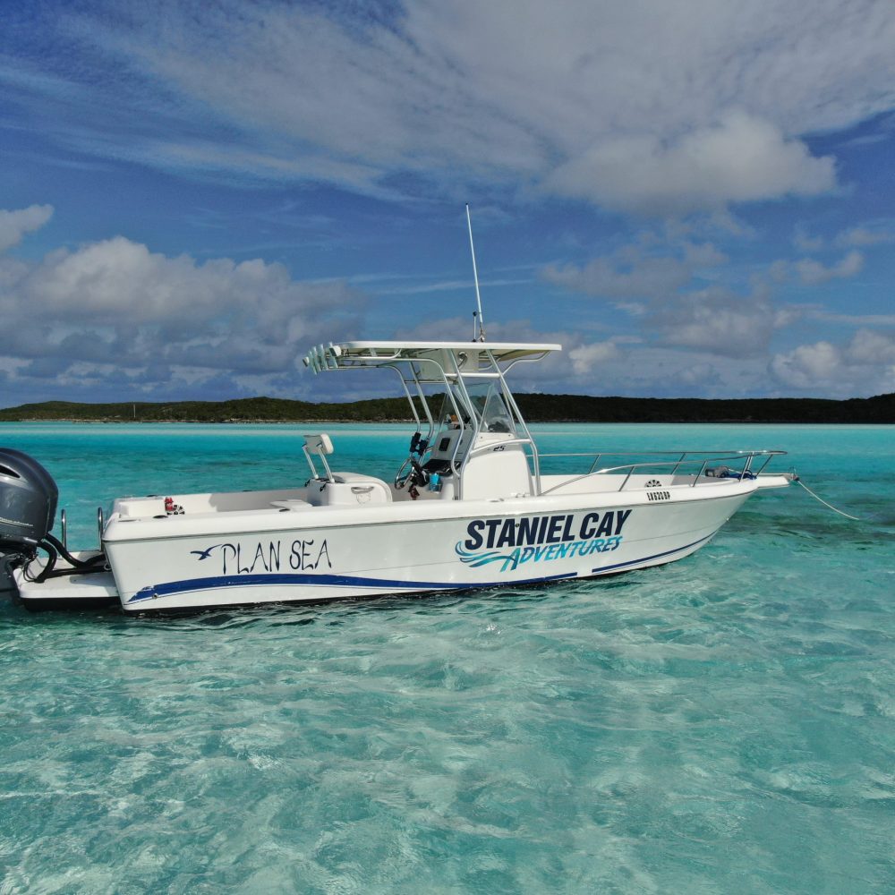 Staniel Cay, Exuma Bahamas A white motorboat labeled "Staniel Cay Adventures" floats on clear turquoise water under a partly cloudy sky.