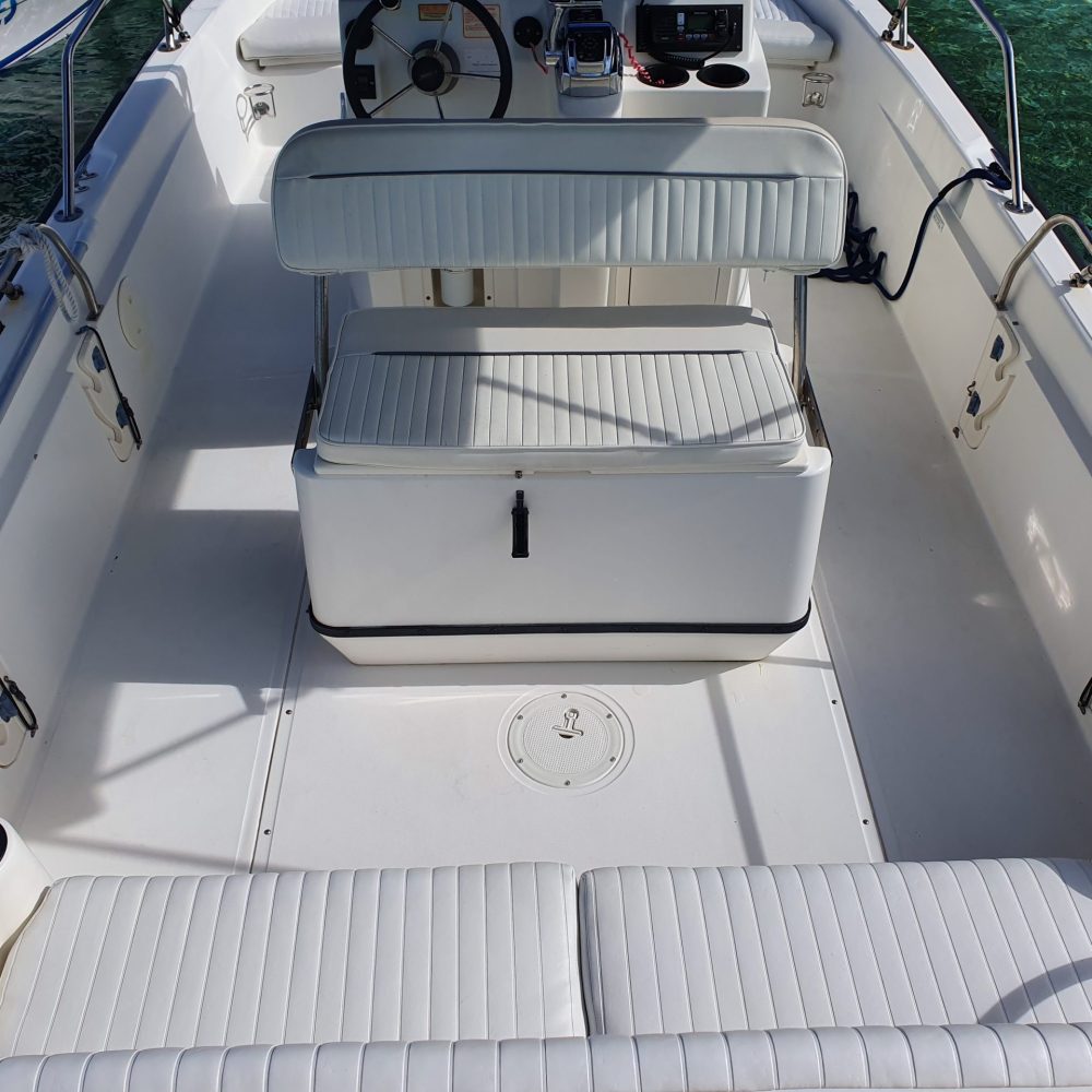 Staniel Cay, Exuma Bahamas View of a white boat's interior with cushioned seating, steering wheel, and electronic equipment, set against a background of clear water.