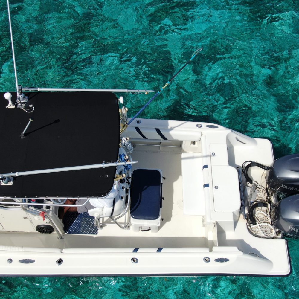 Staniel Cay, Exuma Bahamas A white fishing boat with a black canopy floats on clear turquoise water, featuring two outboard motors and fishing rods.