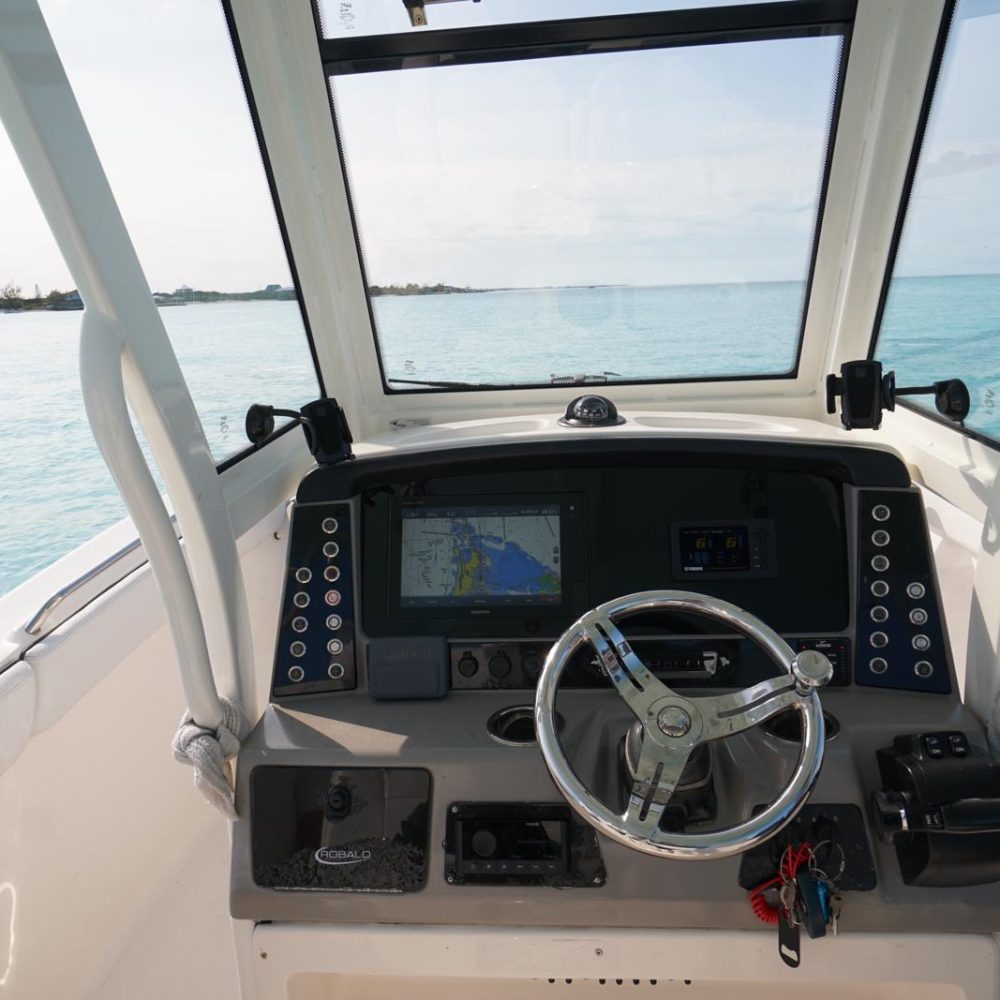 Staniel Cay, Exuma Bahamas Boat cockpit with steering wheel, digital displays, and controls overlooking a calm blue sea under a clear sky.