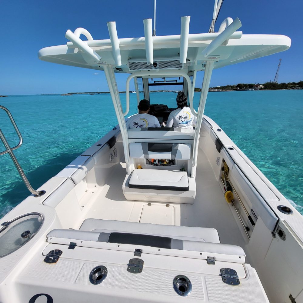 Staniel Cay, Exuma Bahamas View from the back of a boat named "Great Timing," with two people at the helm. The boat is on clear turquoise water under a blue sky.