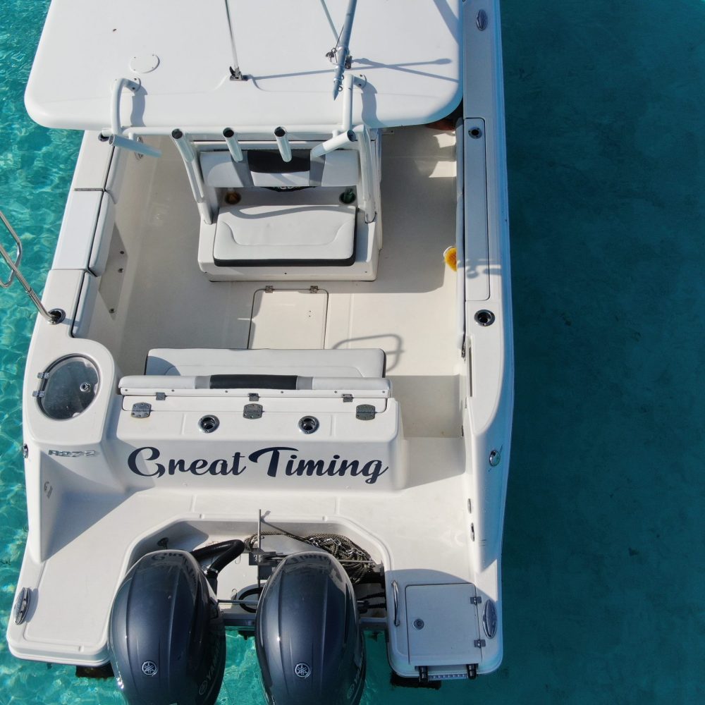 Staniel Cay, Exuma Bahamas Aerial view of a white motorboat named "Great Timing" on clear turquoise water. The boat has twin engines and an open deck layout.