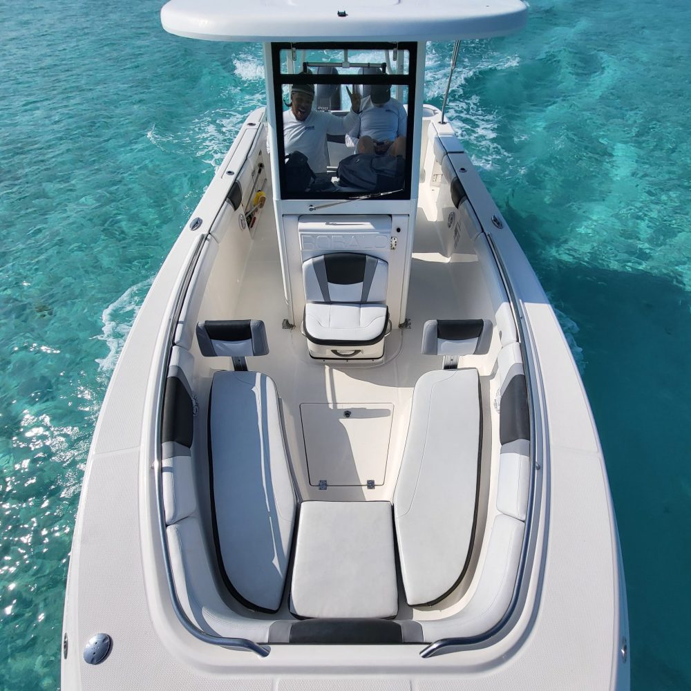 Staniel Cay, Exuma Bahamas Aerial view of a white motorboat with a blue roof cruising on clear turquoise water, showing cushioned seating and two people at the helm.