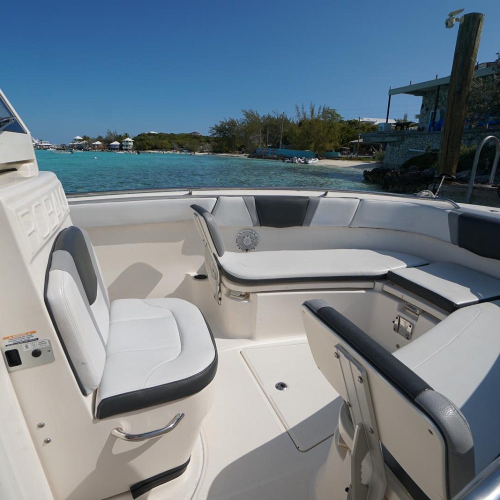 Staniel Cay, Exuma Bahamas Interior view of a small boat with white seating, anchored near a turquoise sea and a shoreline with docks and greenery.