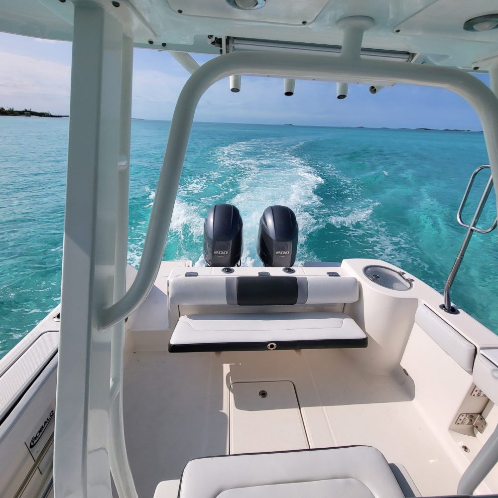 Staniel Cay, Exuma Bahamas The view from the back of a motorboat on clear turquoise water, showing two engines and a wake trailing behind.