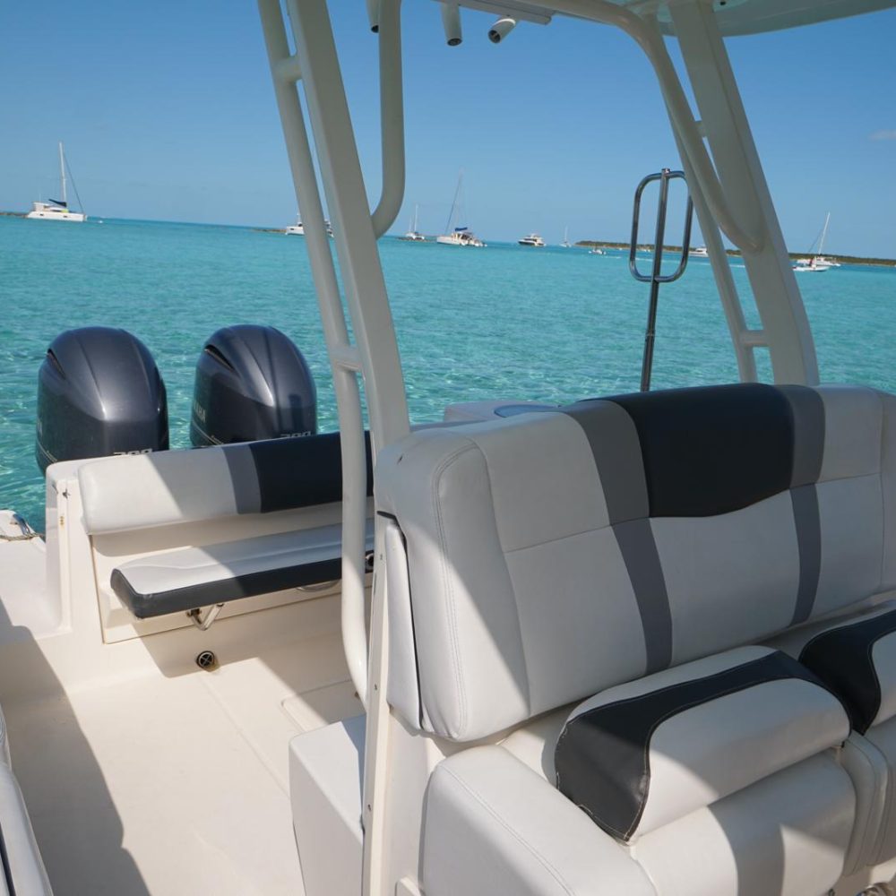 Staniel Cay, Exuma Bahamas View of a boat's seating area with twin engines, surrounded by clear turquoise water and distant anchored boats under a clear blue sky.