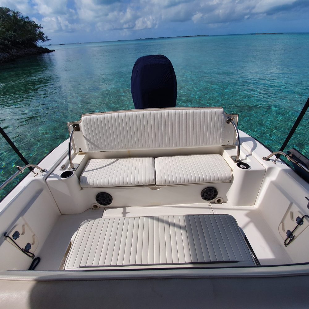 Staniel Cay, Exuma Bahamas Boat seating area with white cushions on clear turquoise water, against a backdrop of distant land and a partly cloudy sky.