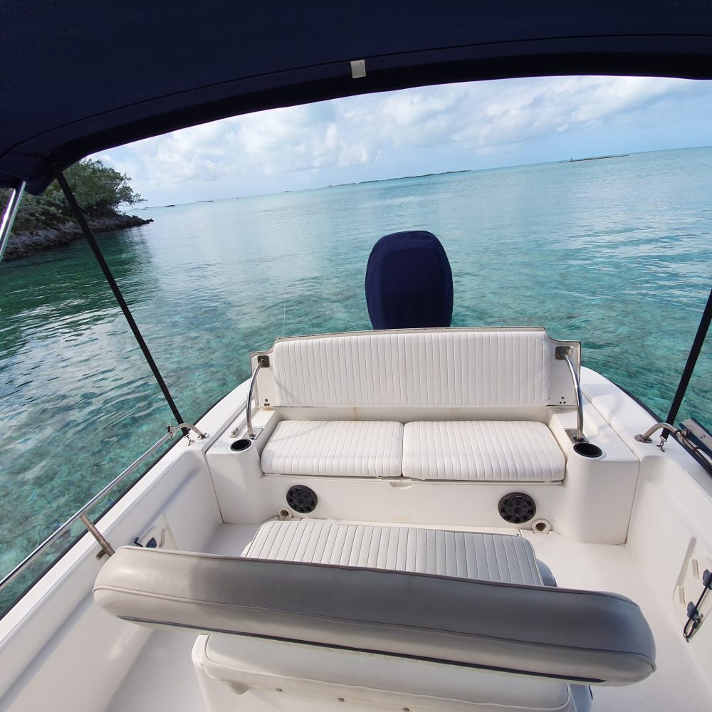 Staniel Cay, Exuma Bahamas View from a boat with white seating, surrounded by clear turquoise water and a partly cloudy sky. Trees are visible on the left side in the background.